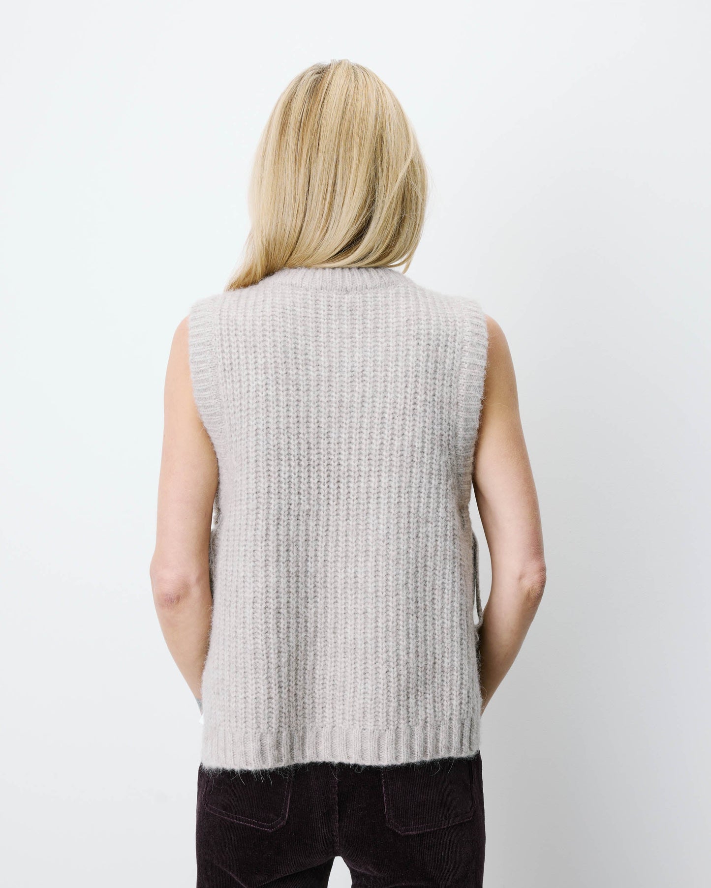 Person wearing a light gray sleeveless knitted vest on a white background