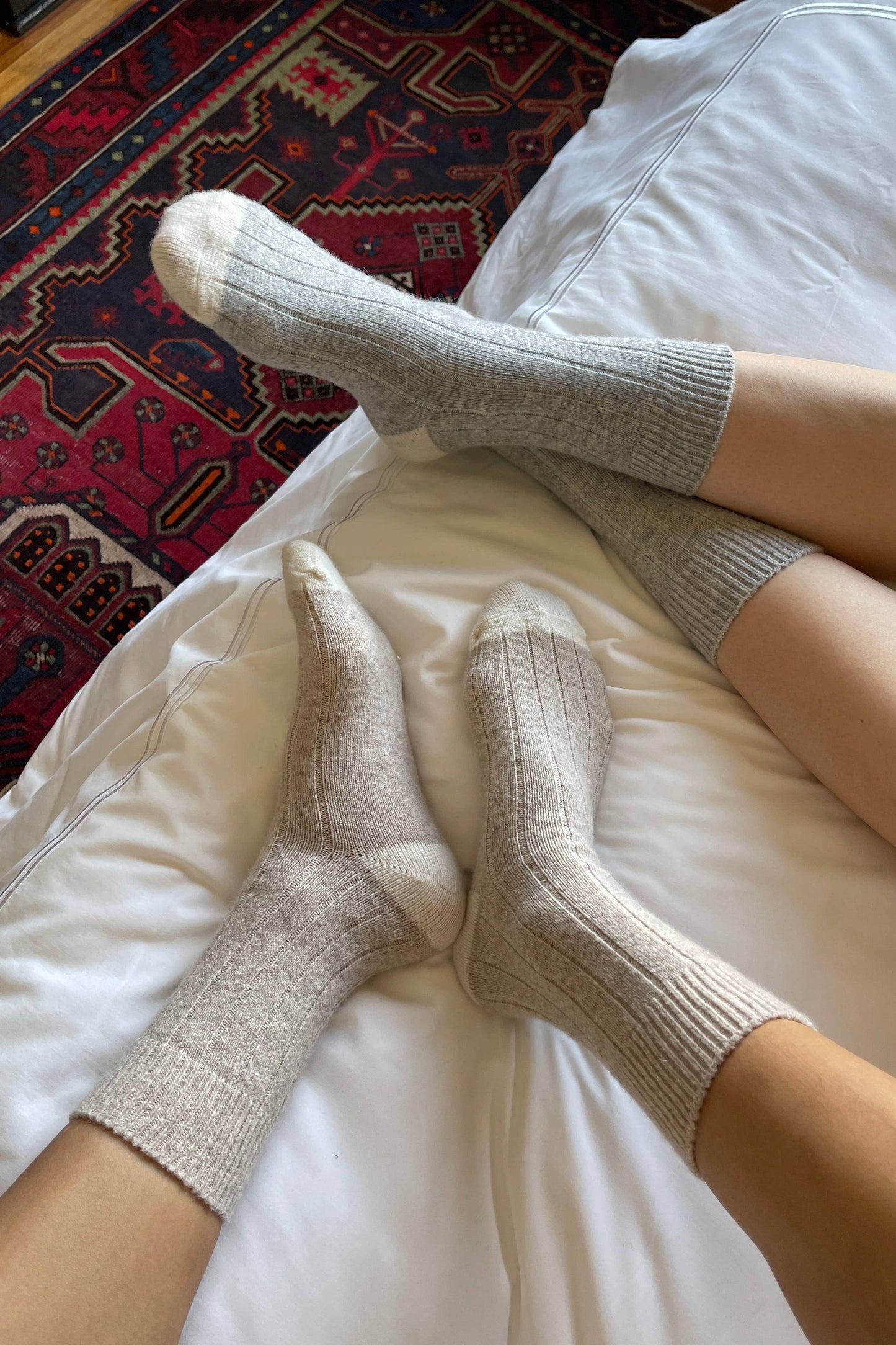 Person wearing gray socks on a bed with a patterned rug in the background
