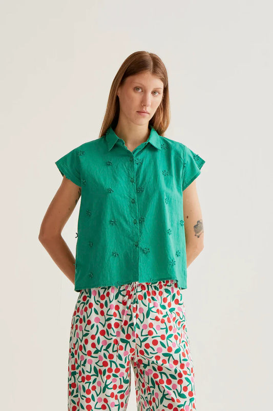 Woman wearing a green patterned shirt and colorful pants on a white background