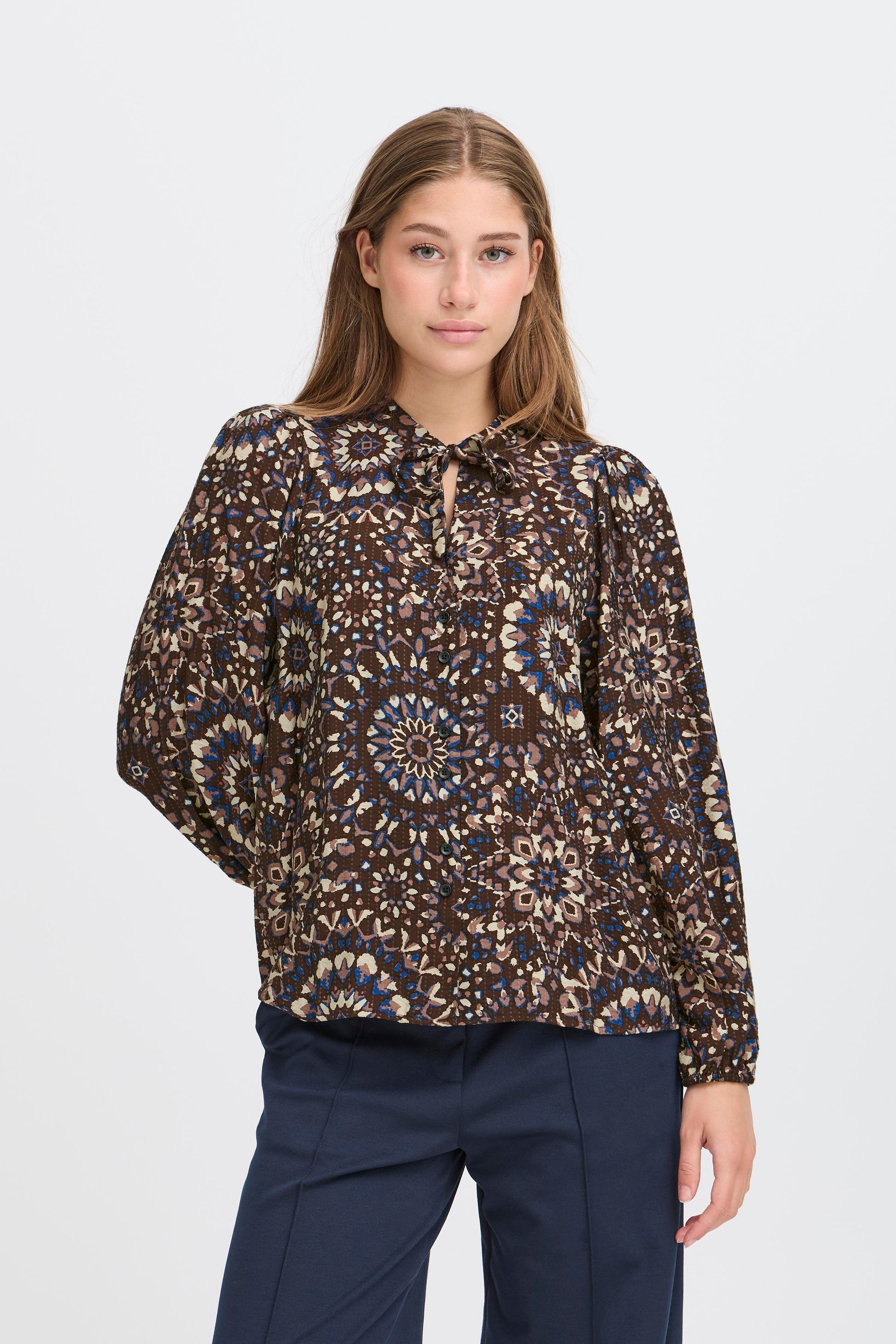 Woman wearing a patterned blouse and navy pants on a white background