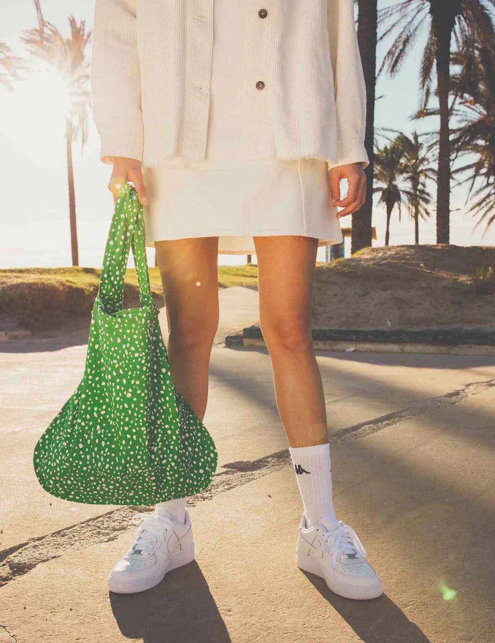 Person holding a green polka dot bag with palm trees in the background