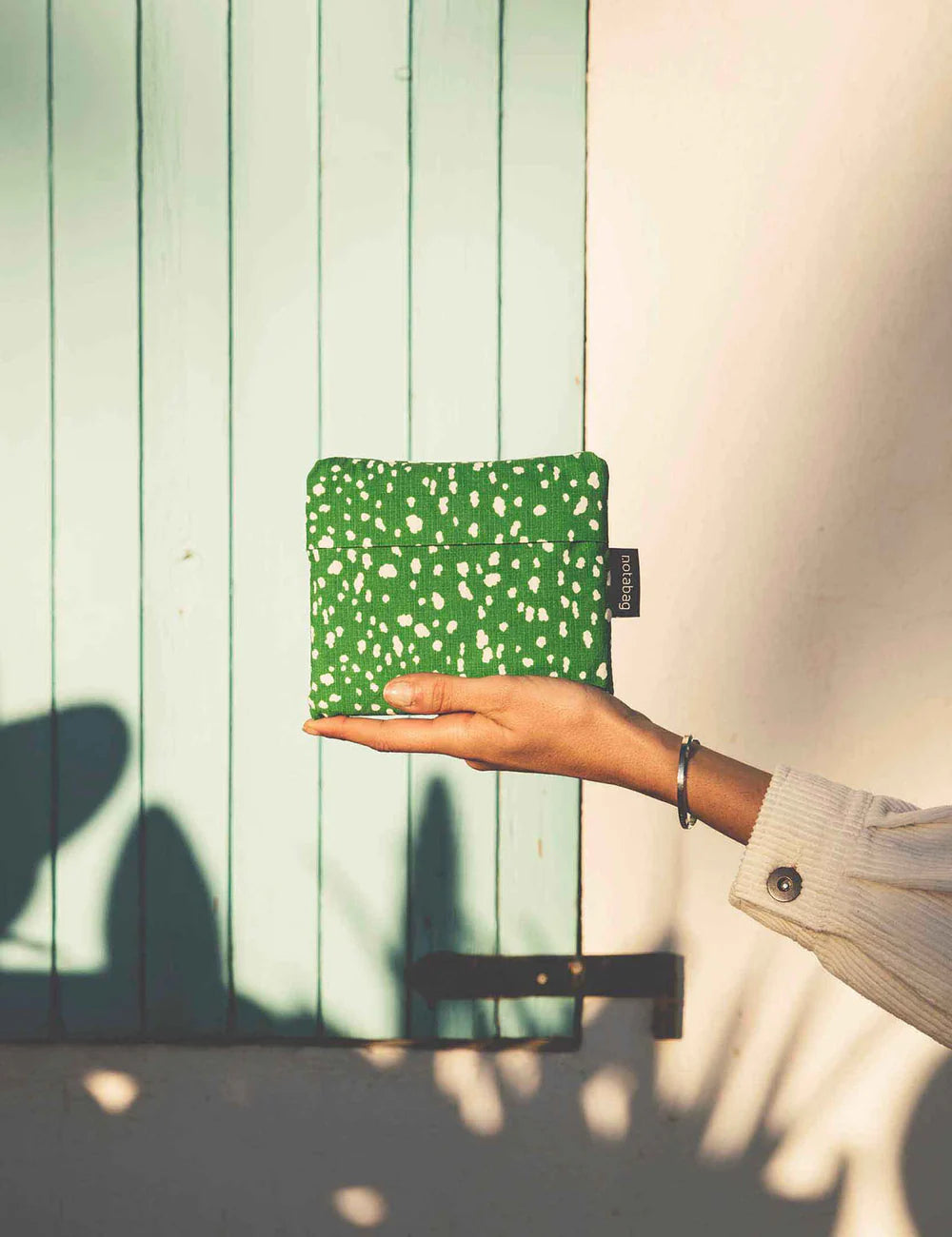Hand holding a green patterned pouch against a light wooden background