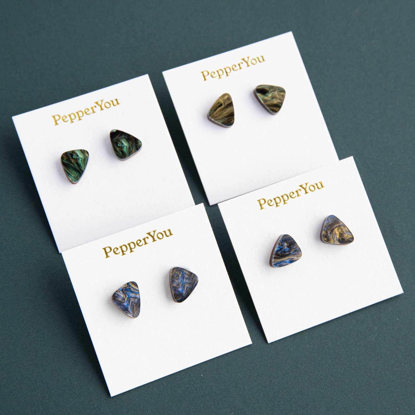 Set of earrings on display with 'PepperYou' branding on white cards against a dark background.