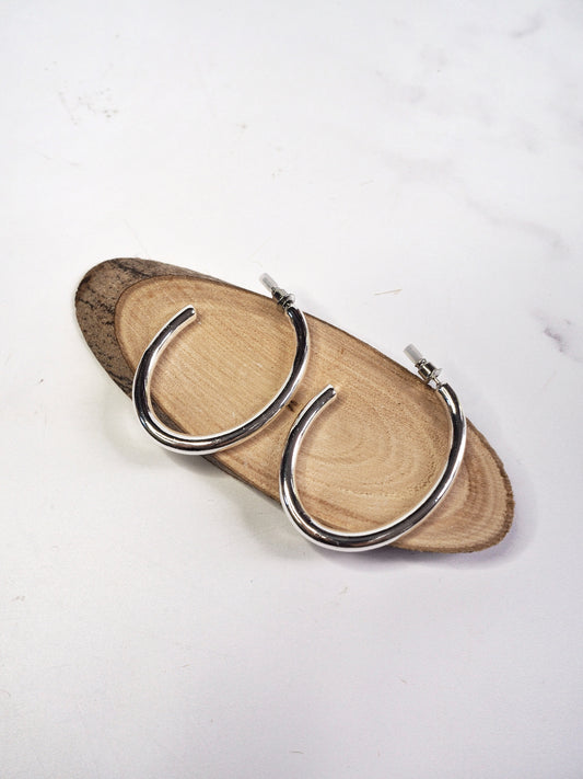 Silver hoop earrings on a wooden stand with a white background