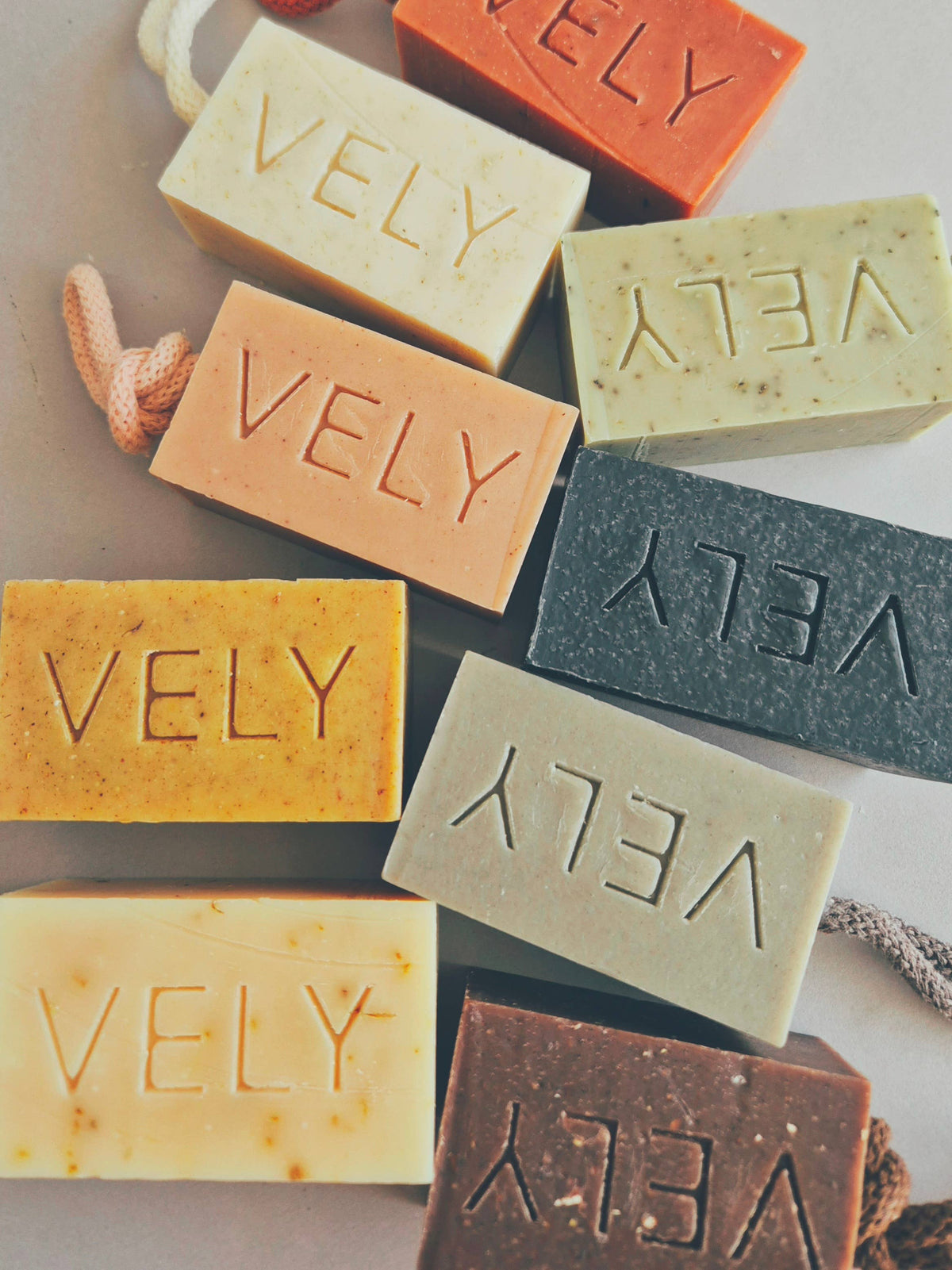 Assorted colored bars of soap with 'VELY' branding on a neutral background