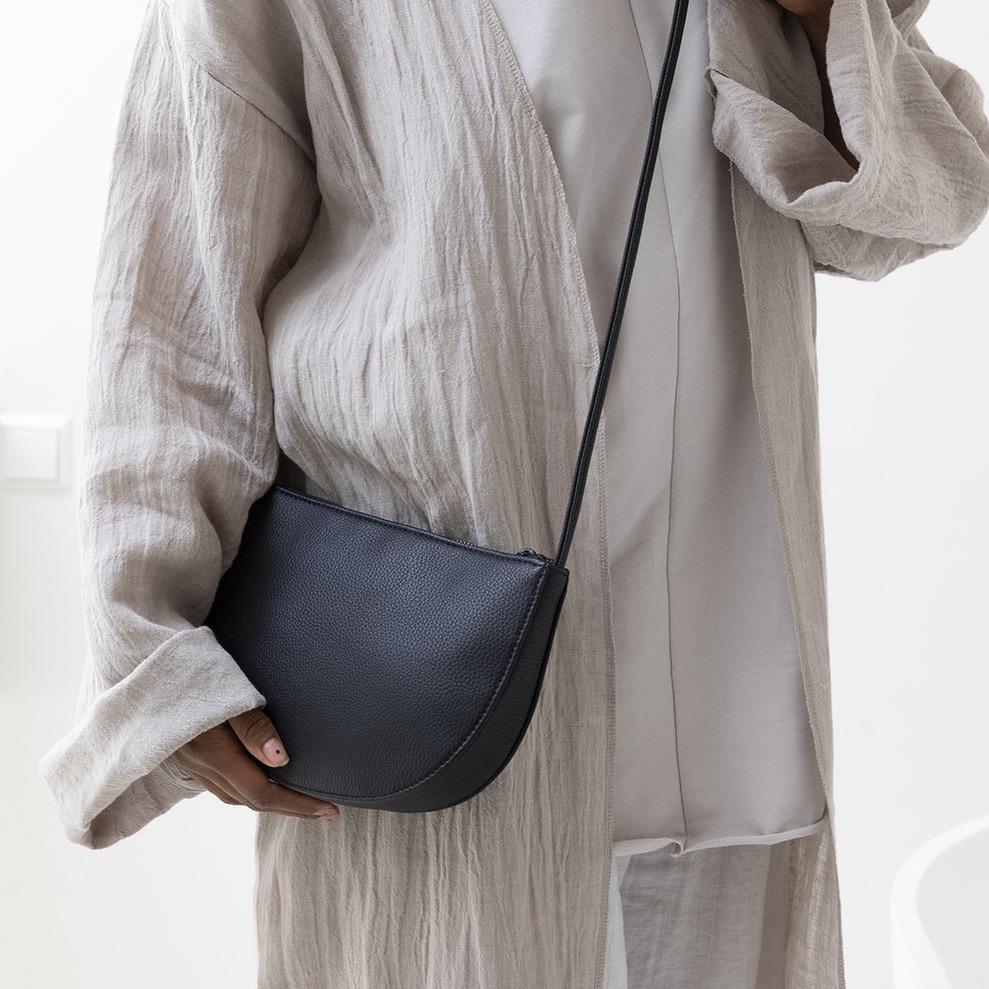 black half moon bag on shoulder of model wearing beige clothing
