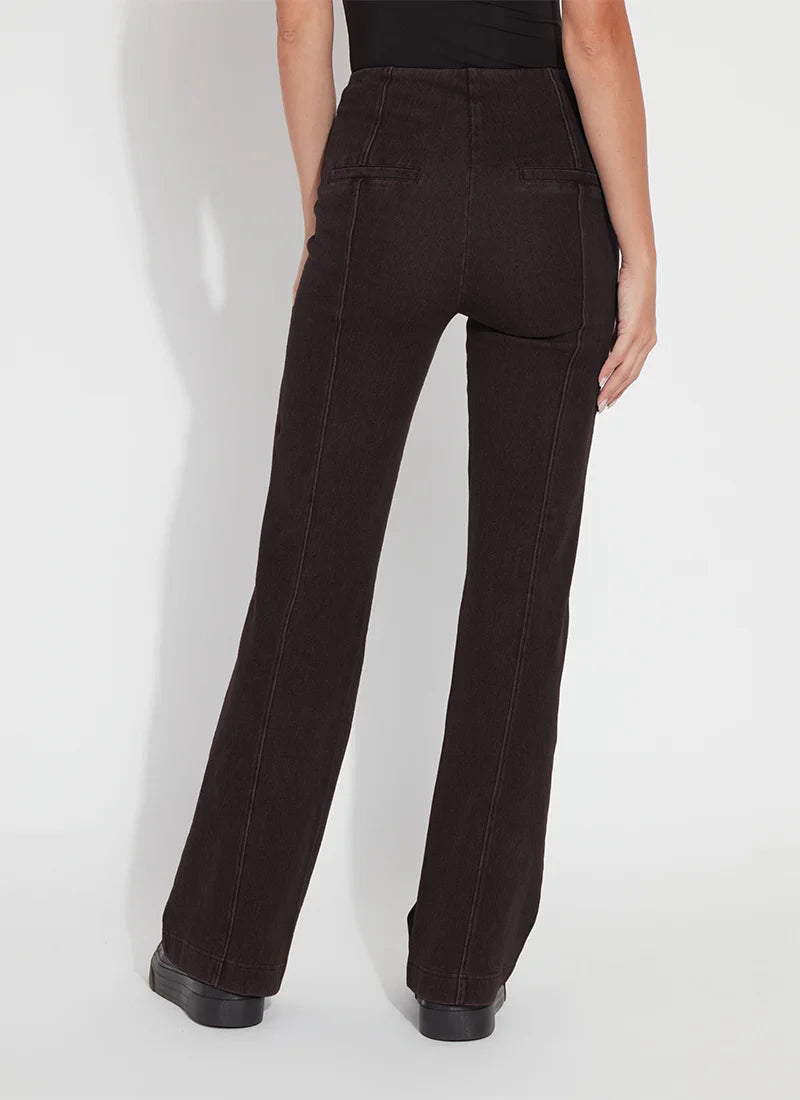 Rear view of a model wearing dark brown wide-leg jeans with a straight-to-slightly-flared leg, paired with a black top and black platform shoes, against a light gray studio background.