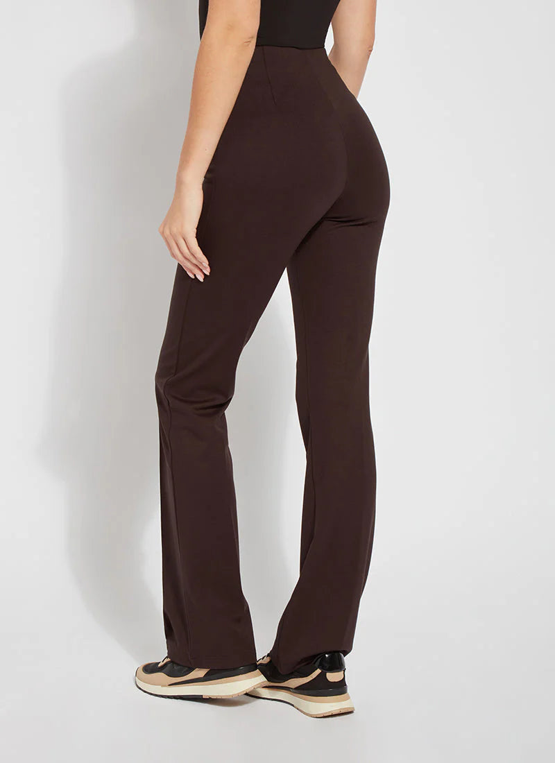 A person shown from the back wearing dark brown high-waisted flared pants with a black top and beige-and-black sneakers, standing against a light gray studio background.