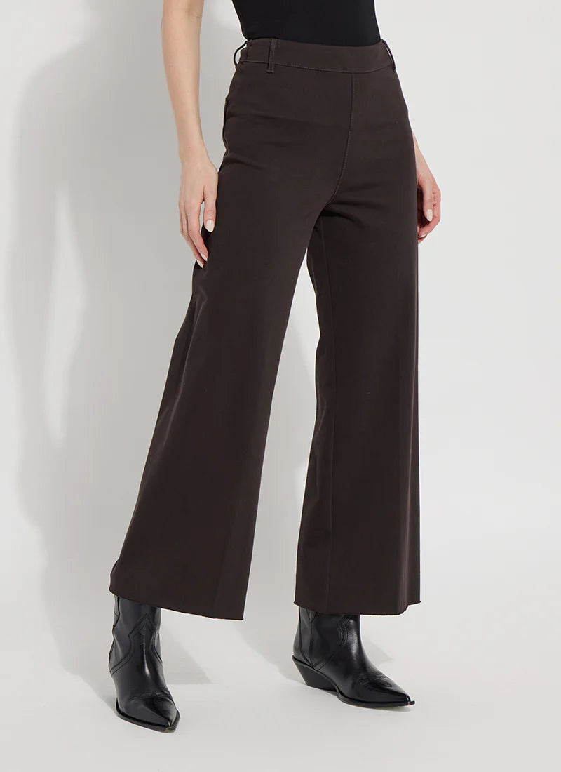 A model wearing dark brown wide-leg cropped trousers, styled with a black top and black pointed-toe ankle boots against a light gray studio background.