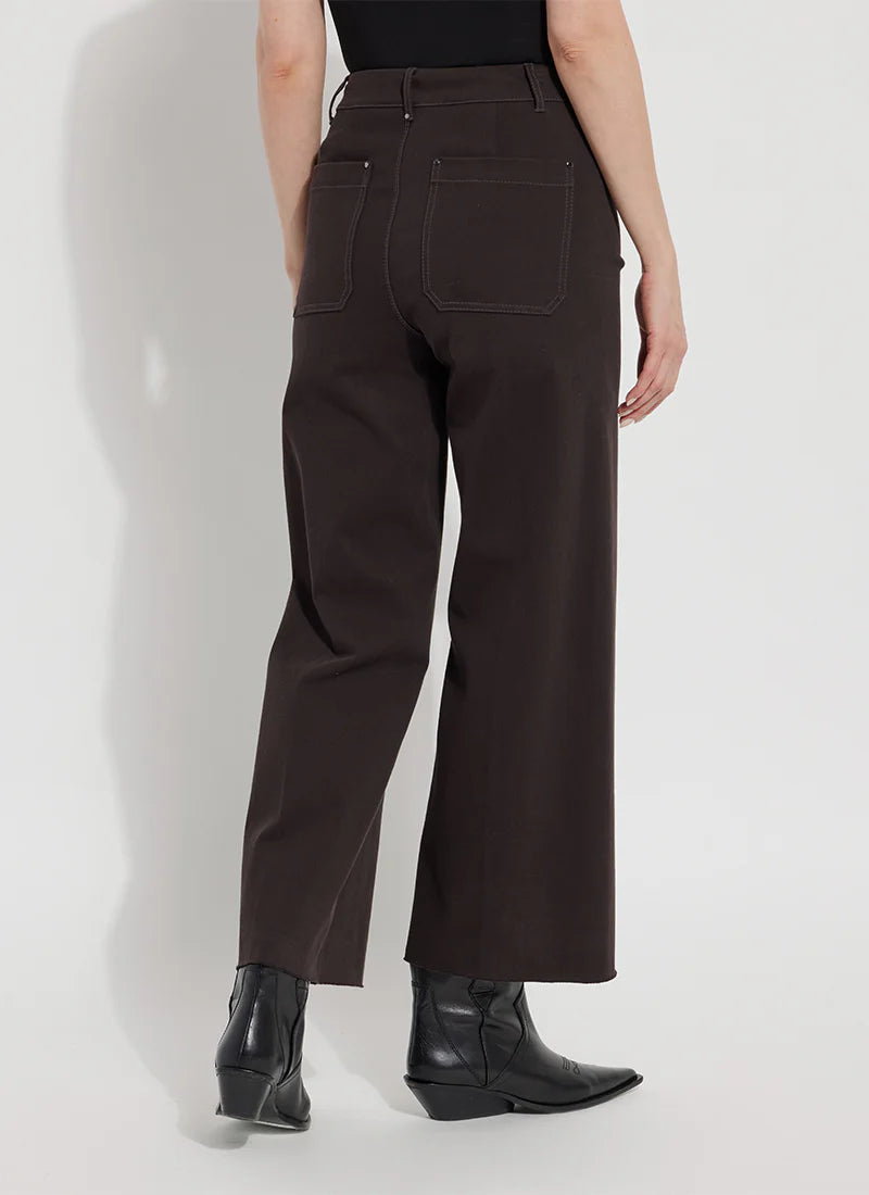 A person shown from the back wearing dark brown wide-leg cropped pants with a black top and black ankle boots, standing against a light gray studio background.