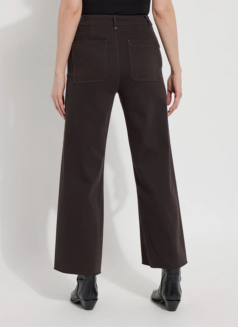 A person shown from the back wearing dark brown wide-leg cropped pants with a black top and black ankle boots, photographed against a plain light studio background.