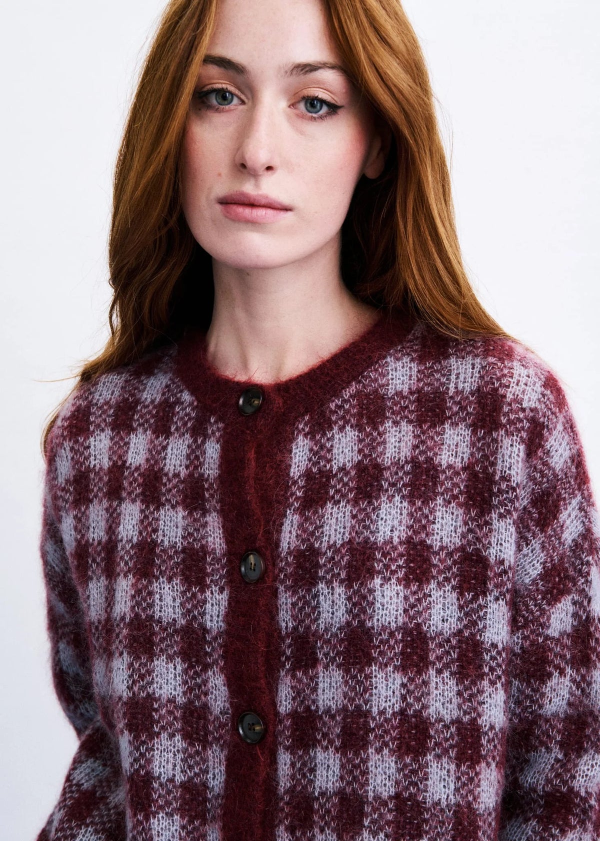 A close-up of a woman wearing a fuzzy knit cardigan with a burgundy and light gray gingham pattern, featuring dark buttons down the front.