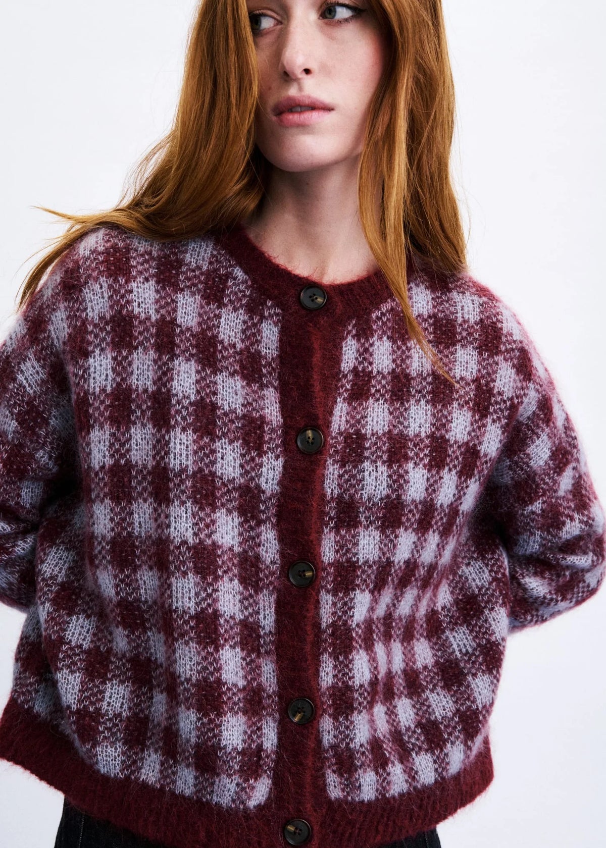 A woman wearing a fuzzy knit cardigan with a burgundy and light gray gingham check pattern, featuring dark buttons down the front.