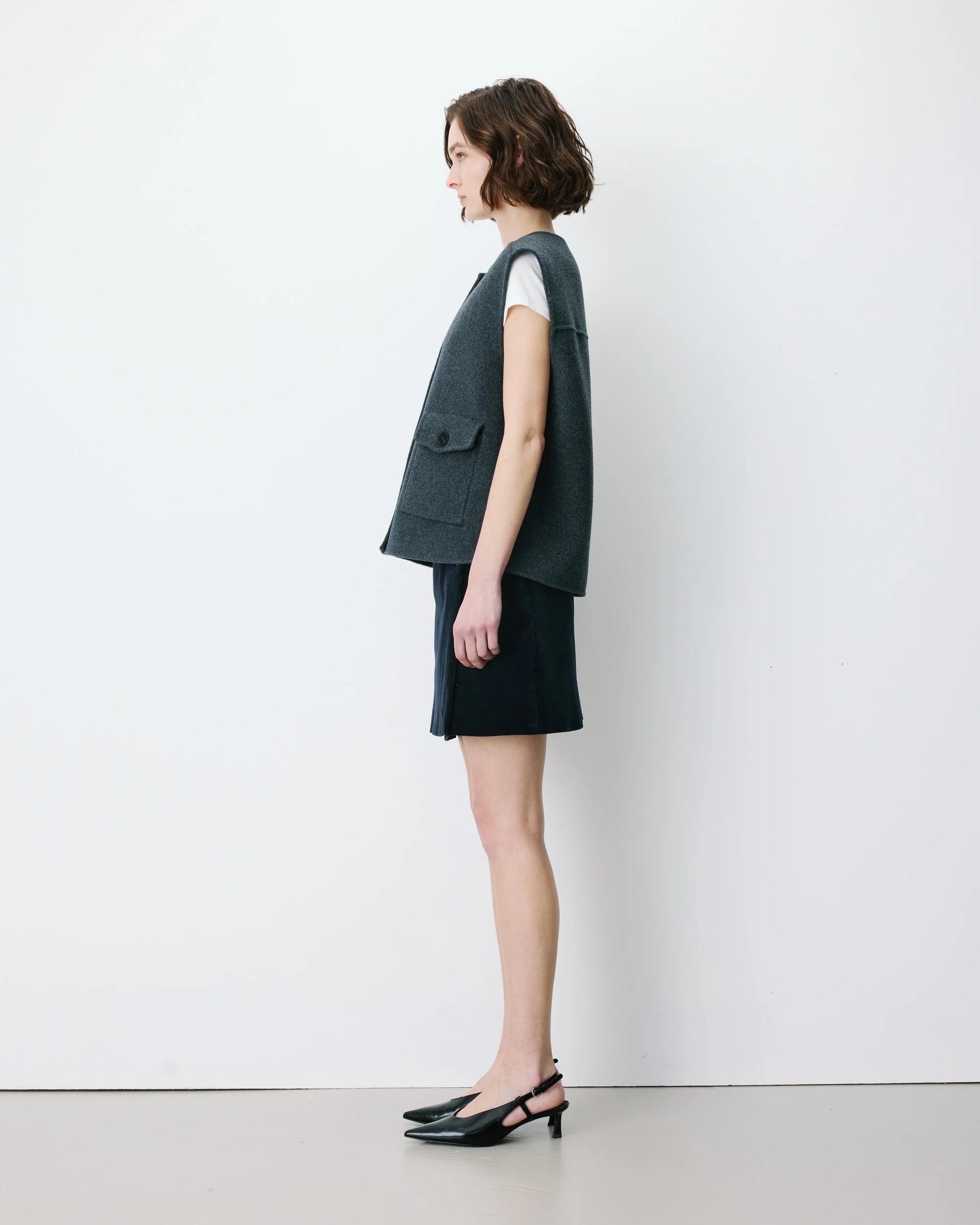Woman wearing a dark green sleeveless top and black skirt against a white background
