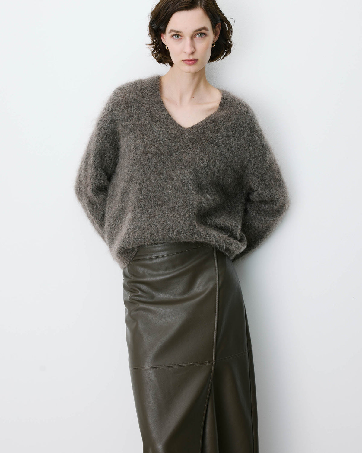 Person wearing a gray sweater and black leather skirt against a white background