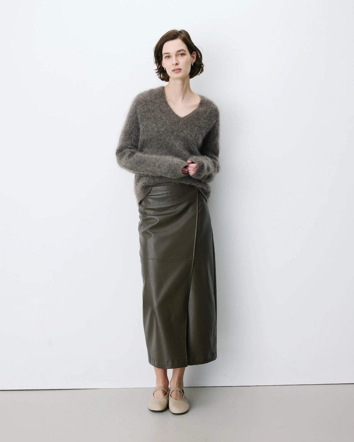 Woman wearing a gray sweater and green leather skirt against a white background
