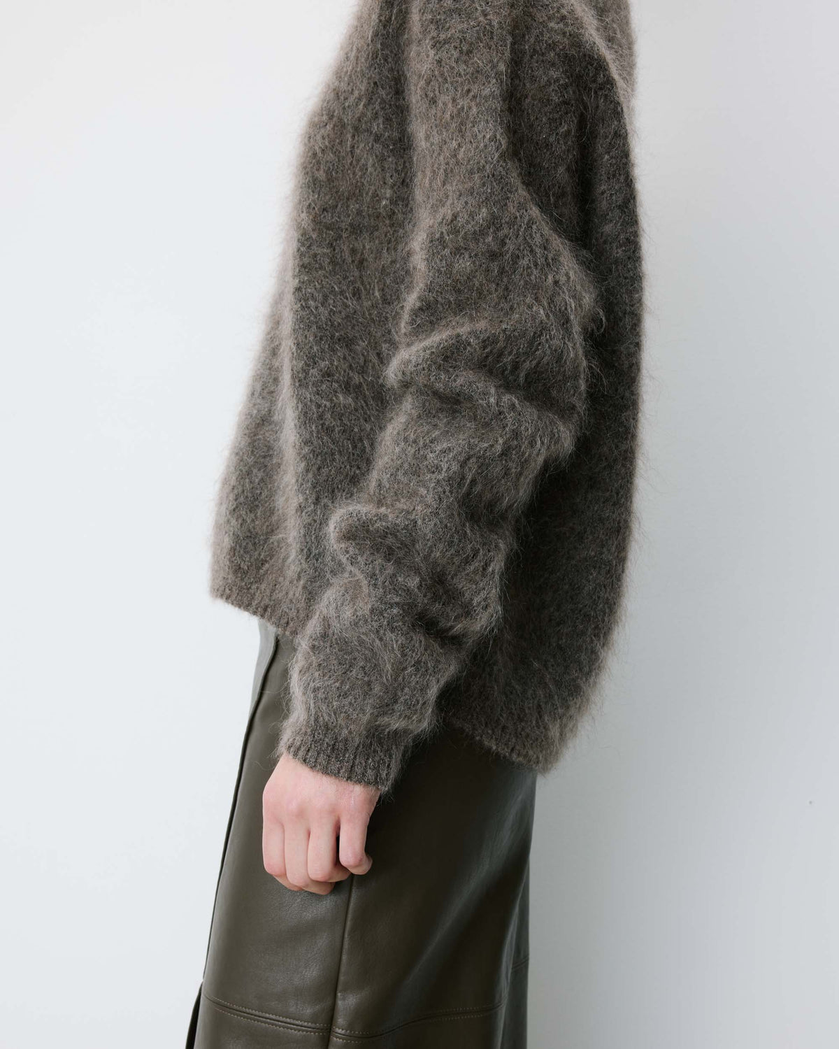 Person wearing a textured gray sweater and green leather pants against a white background
