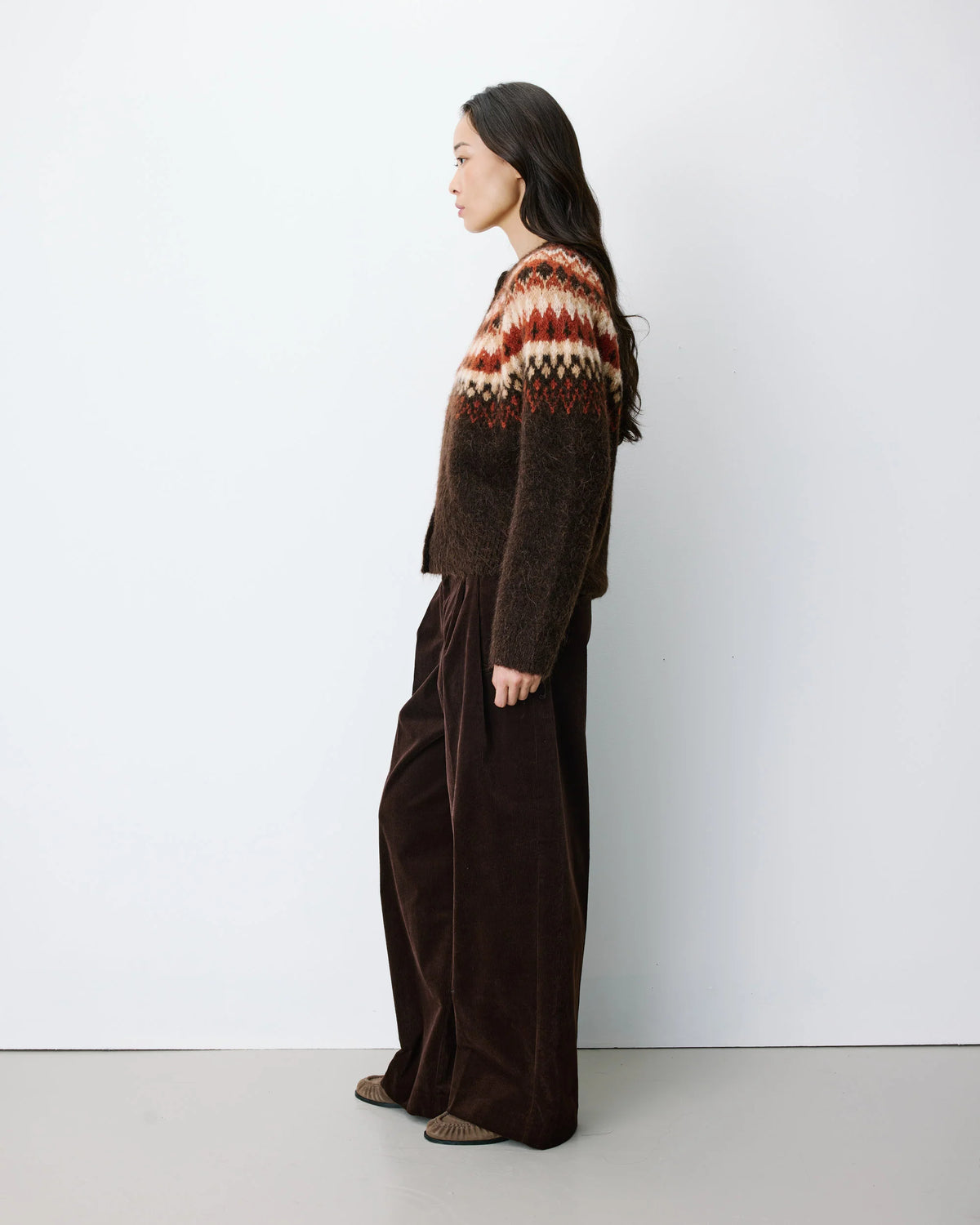 Person wearing a patterned sweater and dark pants against a white background