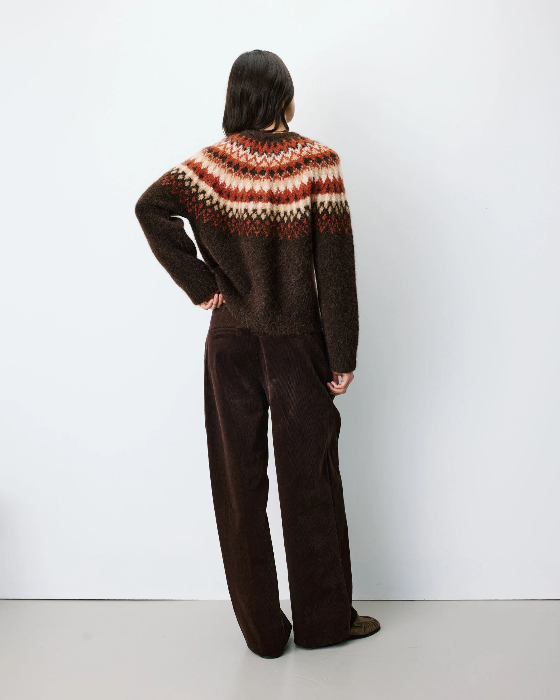 Person wearing a brown patterned sweater and pants against a white background