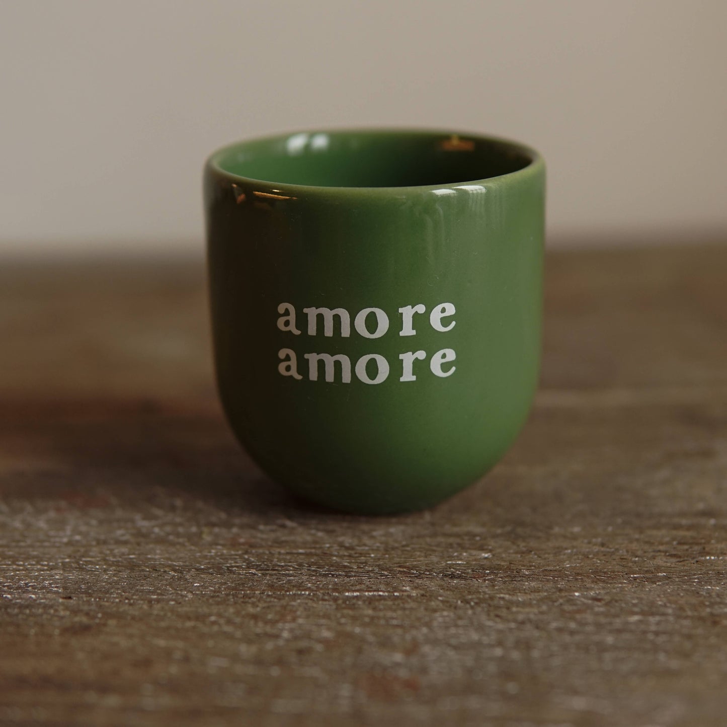 Green ceramic cup with 'amore amore' text on a wooden surface