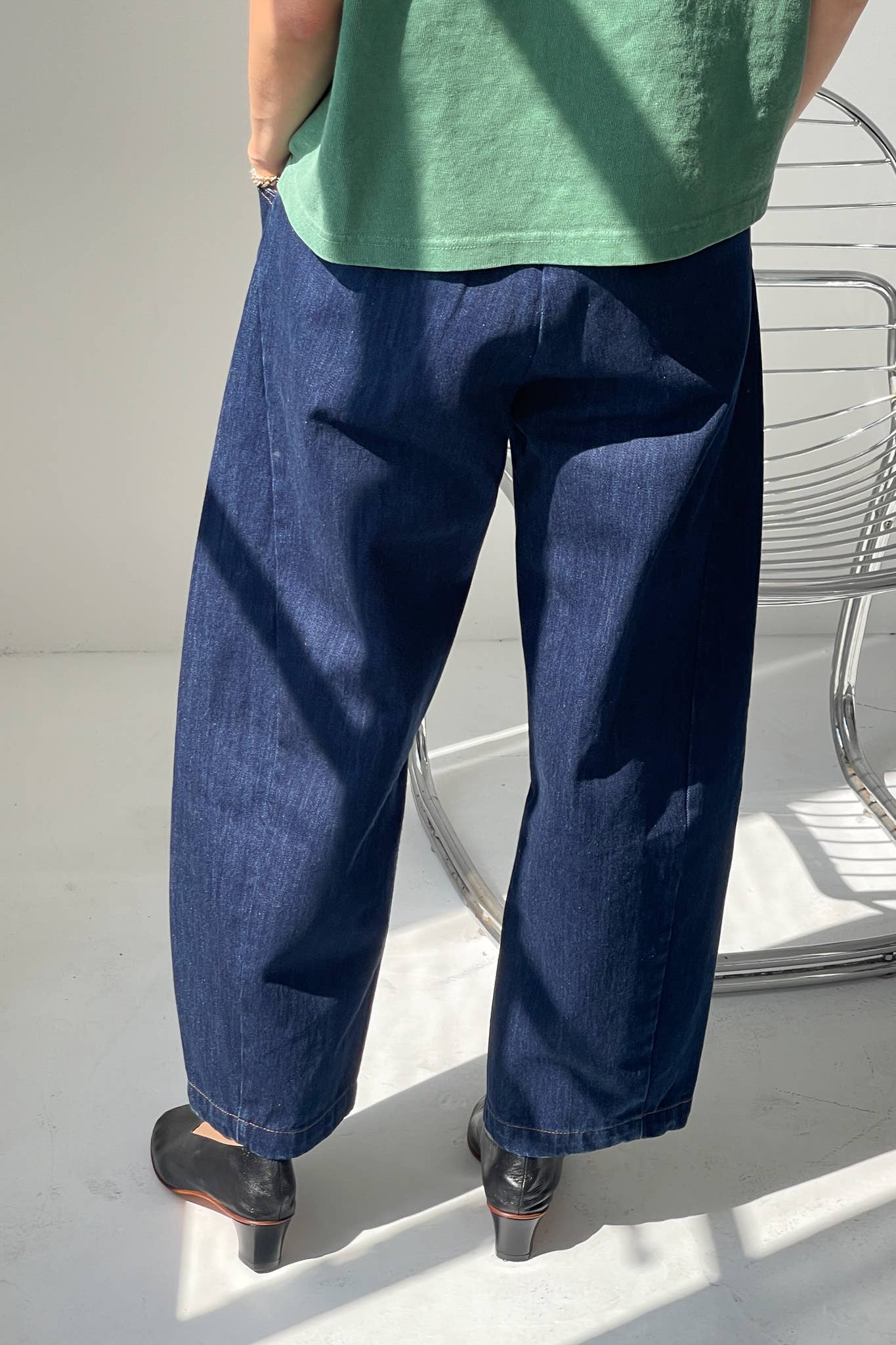 Person wearing blue jeans and a green top on a light background