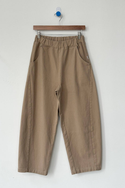 Beige pants hanging on a wooden hanger against a white background