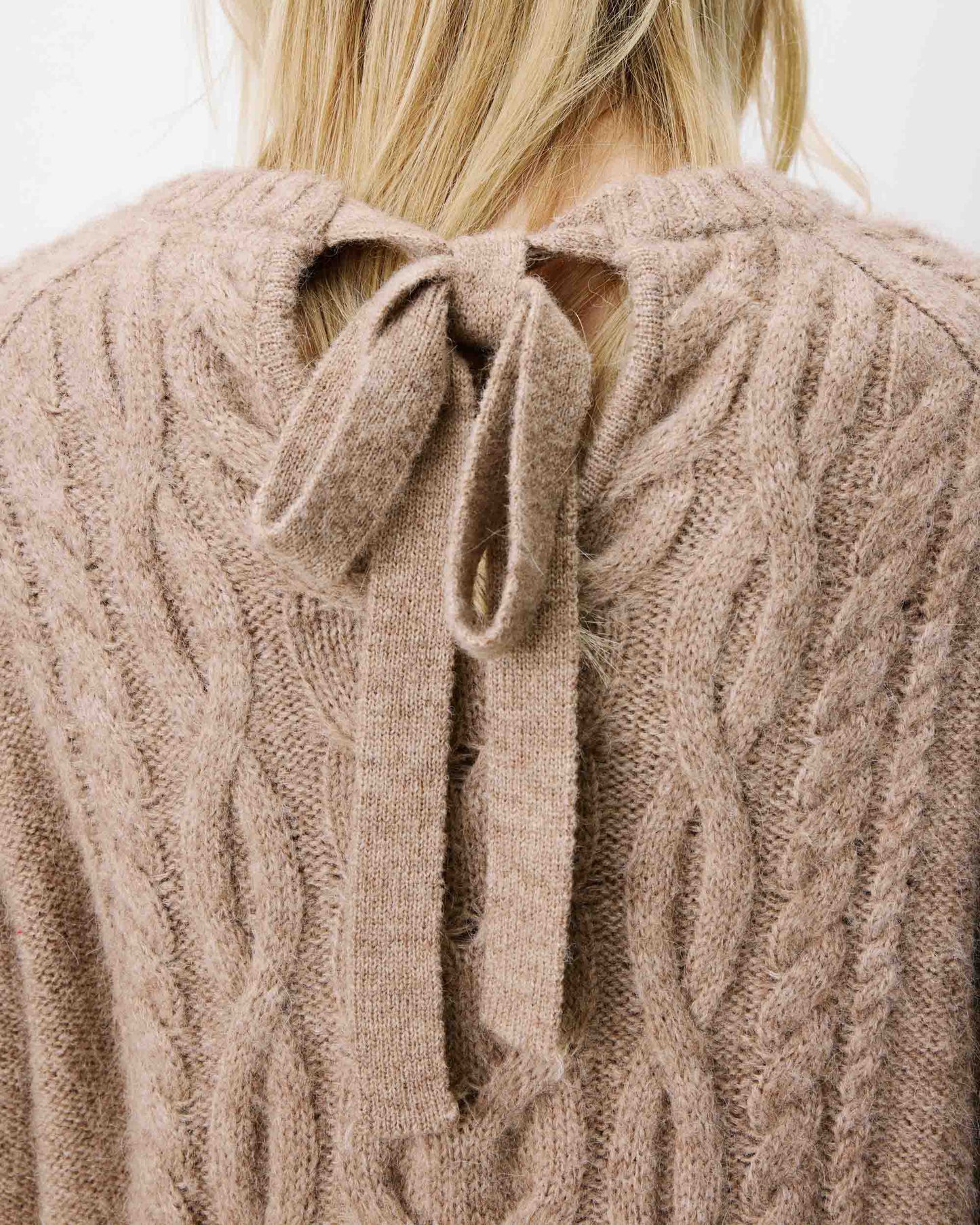 Close-up of a beige cable knit sweater with a bow detail on a plain background