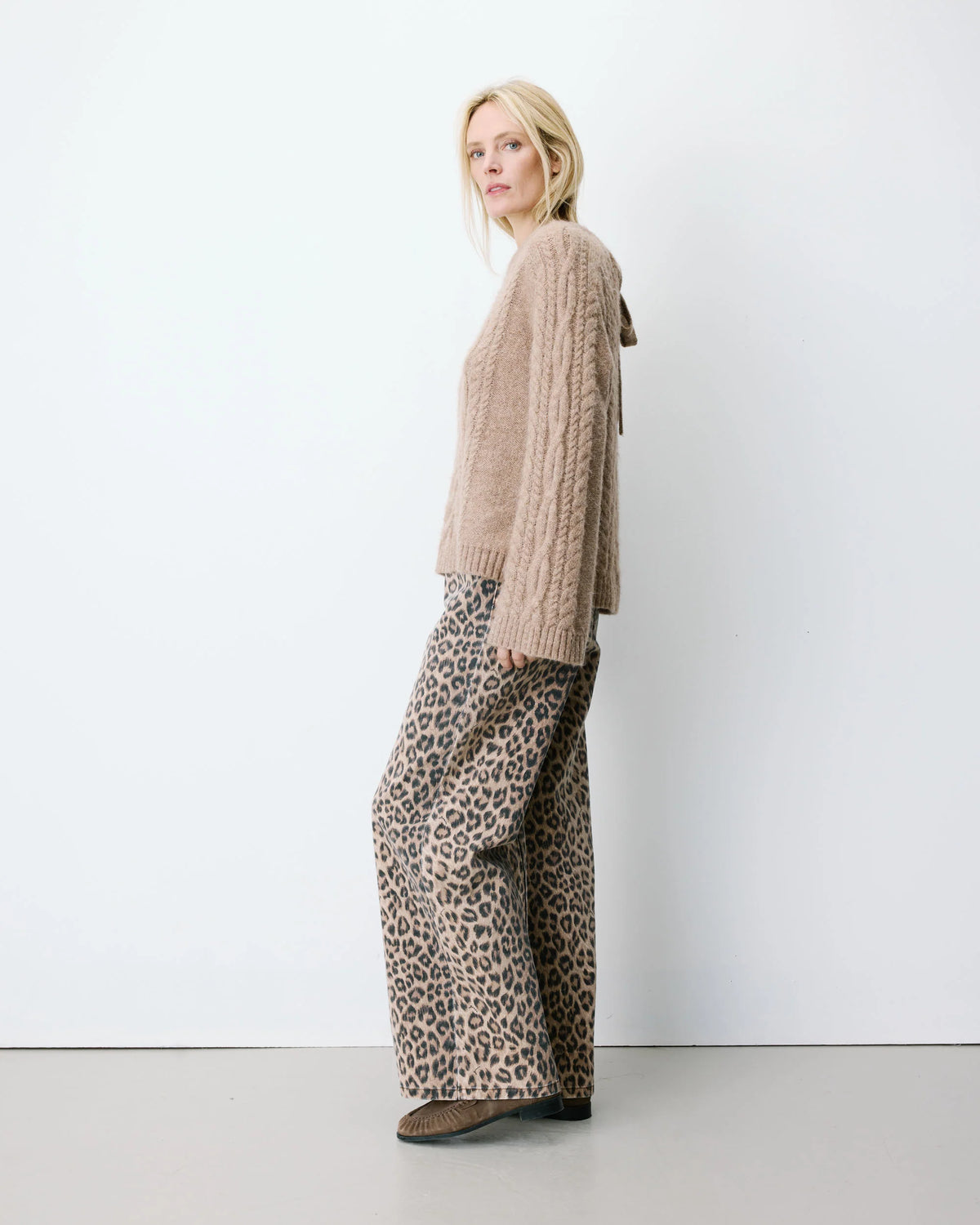 Woman wearing a beige sweater and leopard print pants against a white background
