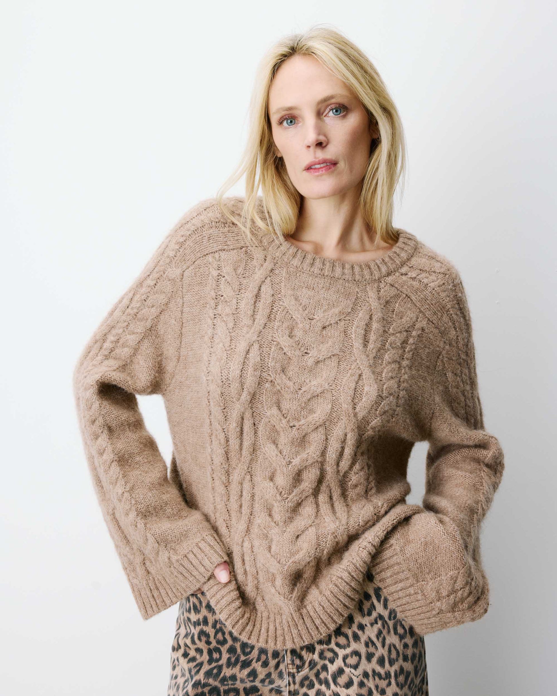 Woman wearing a beige cable knit sweater against a plain background