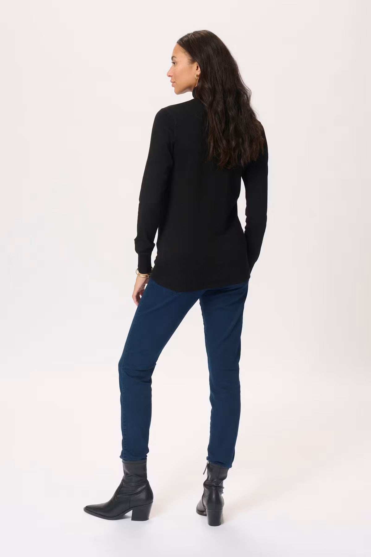 Woman wearing a black long-sleeve top and blue jeans on a white background