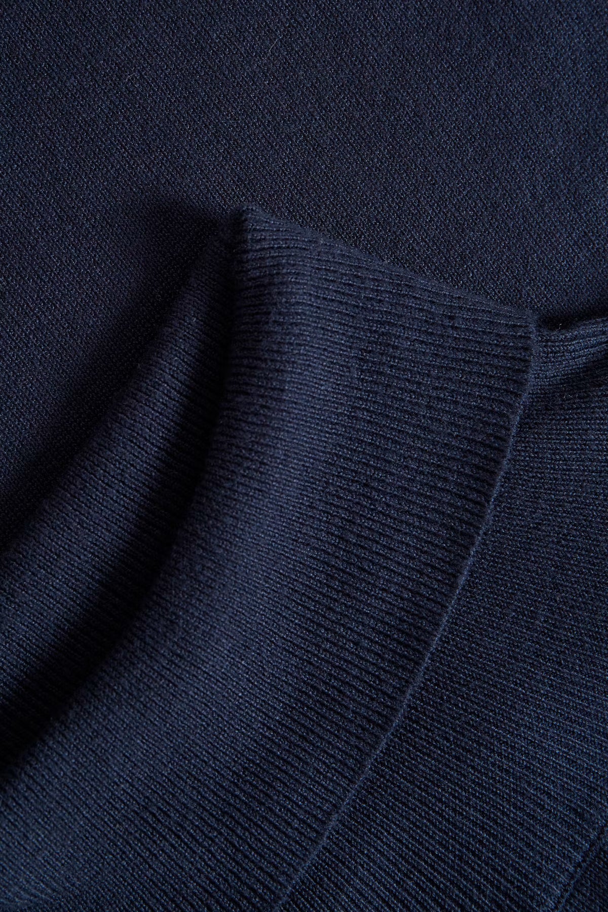 Close-up of a dark navy ribbed knit fabric with a folded corner showing the texture and stitching.