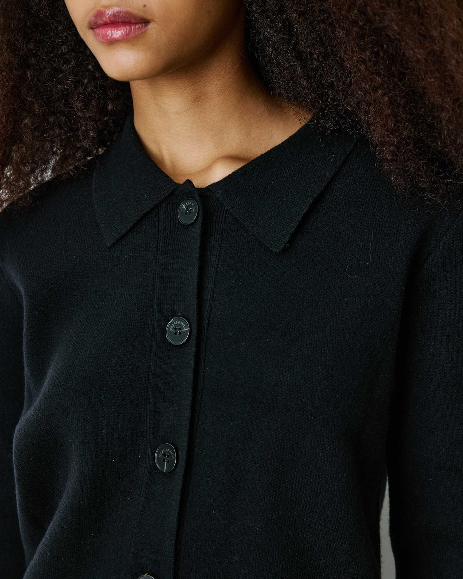 Close-up of a person wearing a black knit collared button-front top or cardigan, showing the collar, front buttons, and part of the neck and hair.