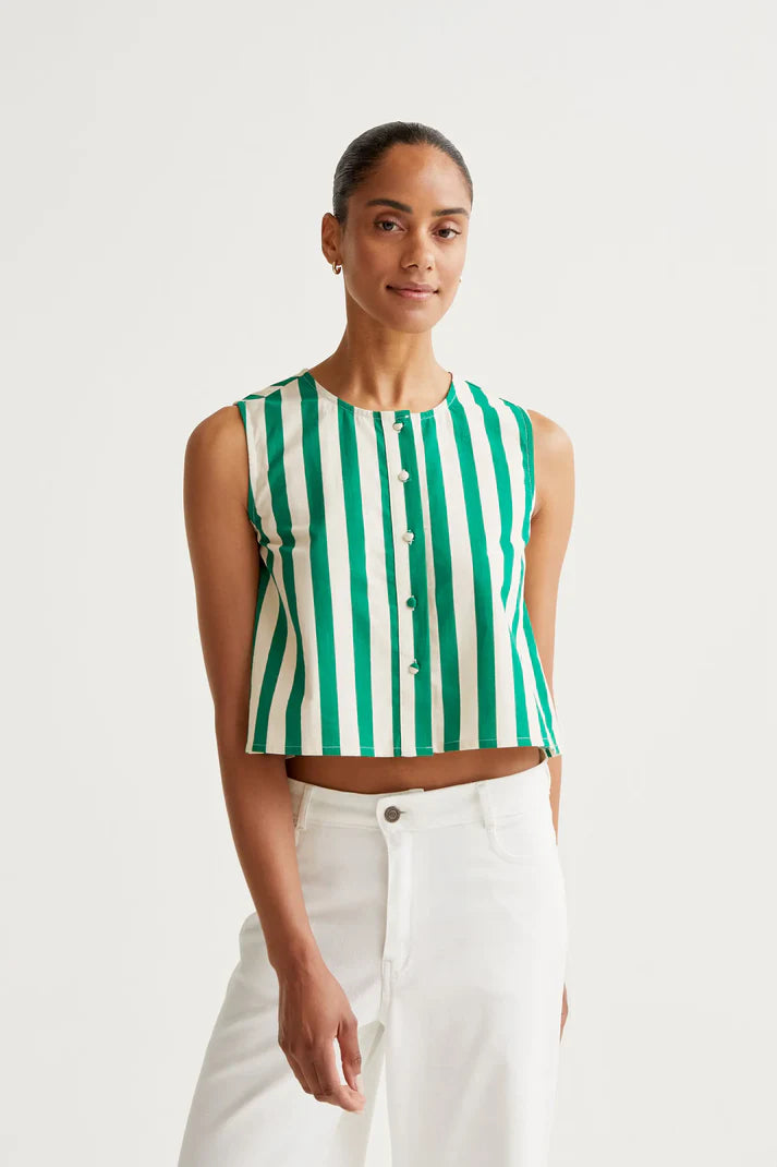 Woman wearing a green and white striped sleeveless top with white pants on a light gray background
