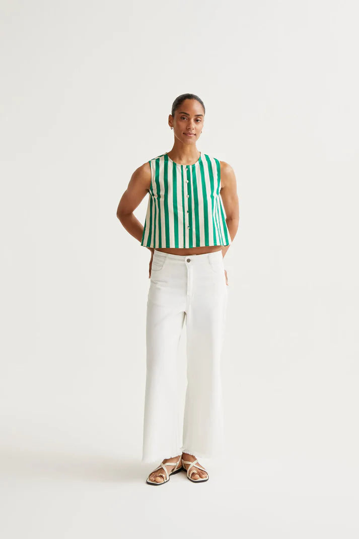 Woman wearing a green and white striped sleeveless top with white pants on a light gray background