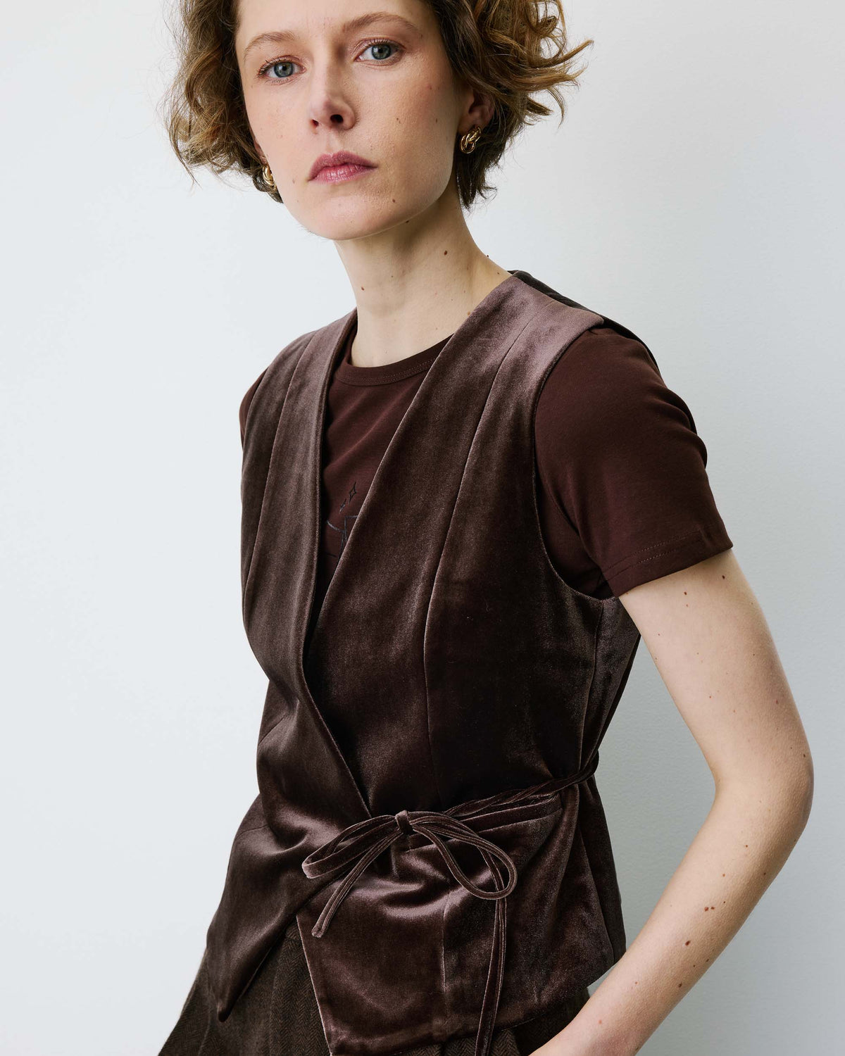 A model wearing a dark brown velvet sleeveless wrap vest over a matching brown t-shirt, set against a plain light gray background.