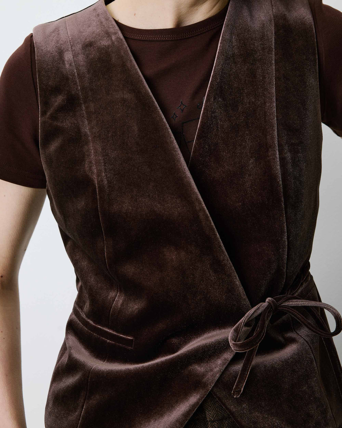 A close-up of a person wearing a dark brown velvet wrap vest over a matching brown t-shirt, against a light gray background.