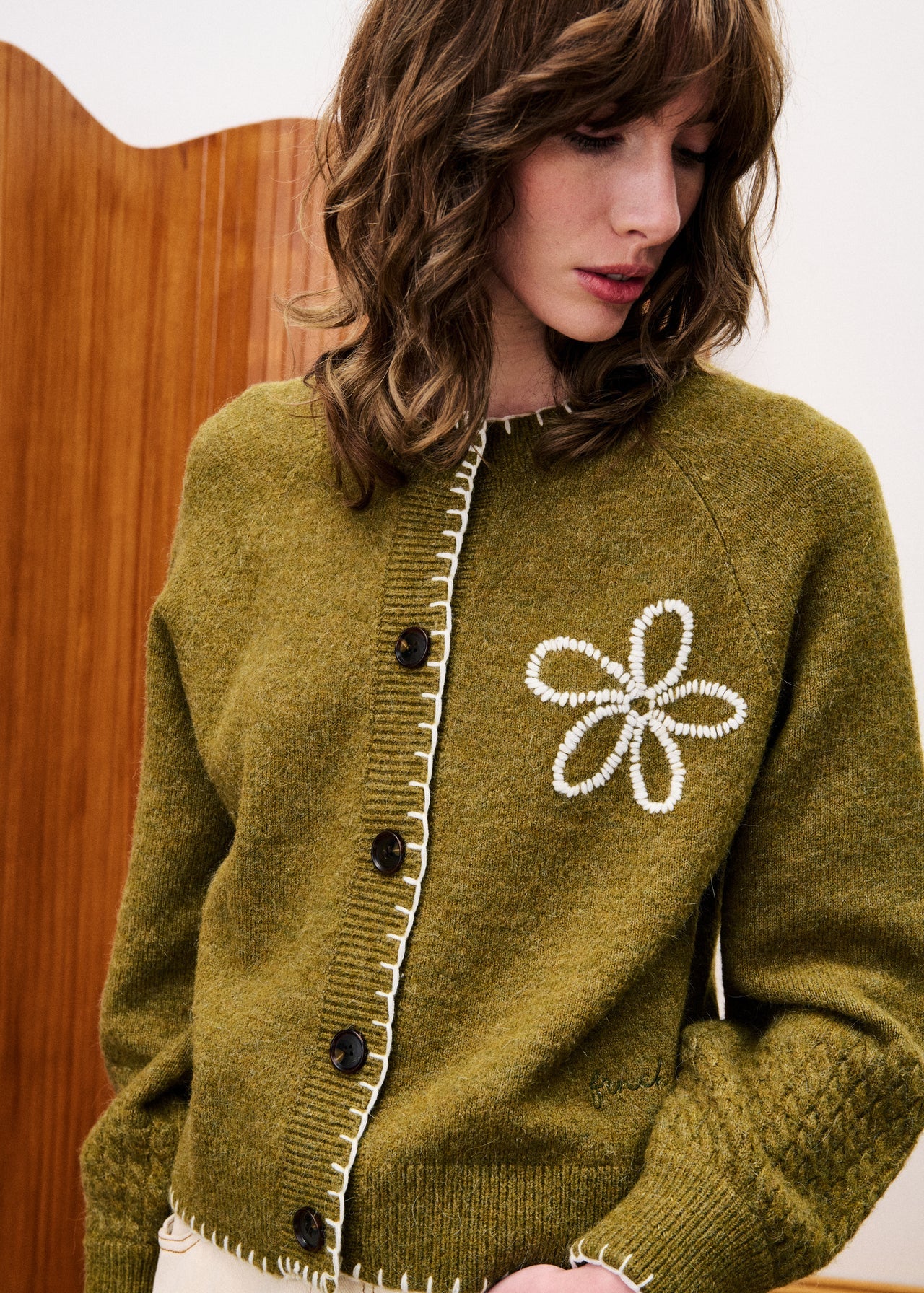 Woman wearing a green cardigan with a floral design and buttons.
