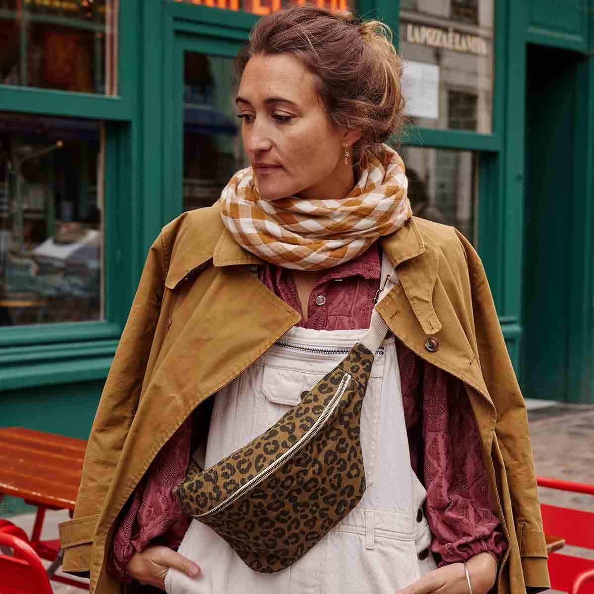 Woman wearing a tan jacket, patterned scarf, and leopard print bag in an urban setting.
