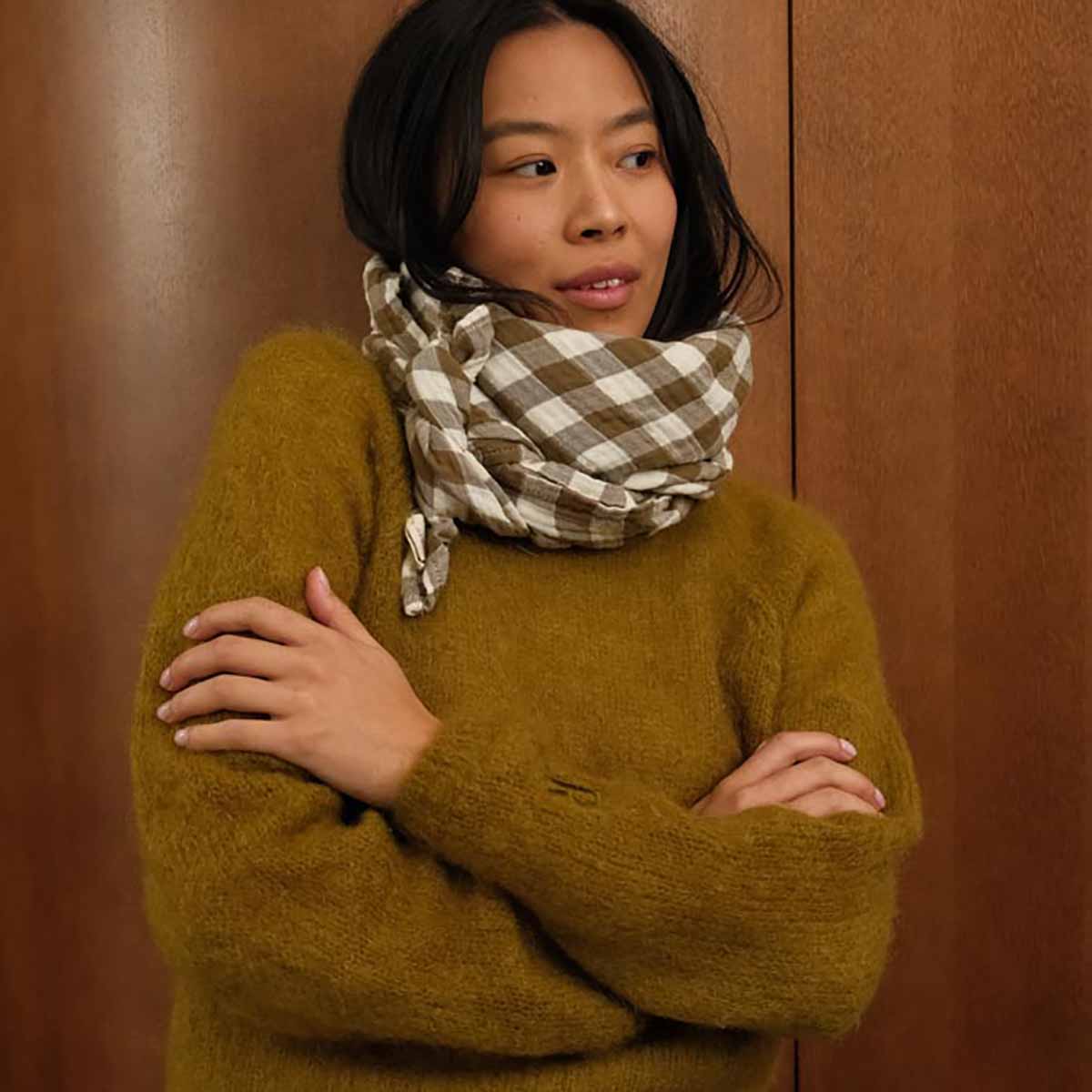 Woman wearing a green sweater and plaid scarf against a brown background