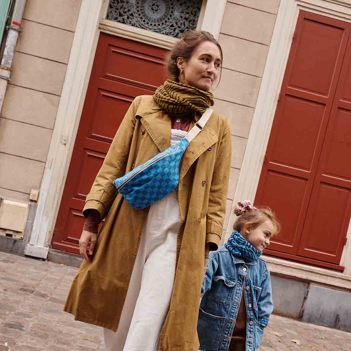 Woman and child walking together on a street with red doors in the background