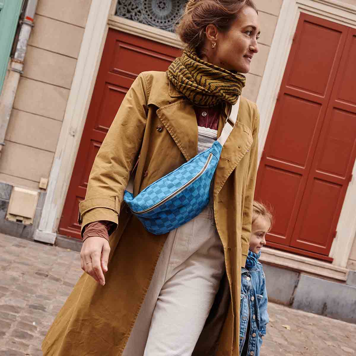 Woman in a brown coat with a blue bag walking outdoors.