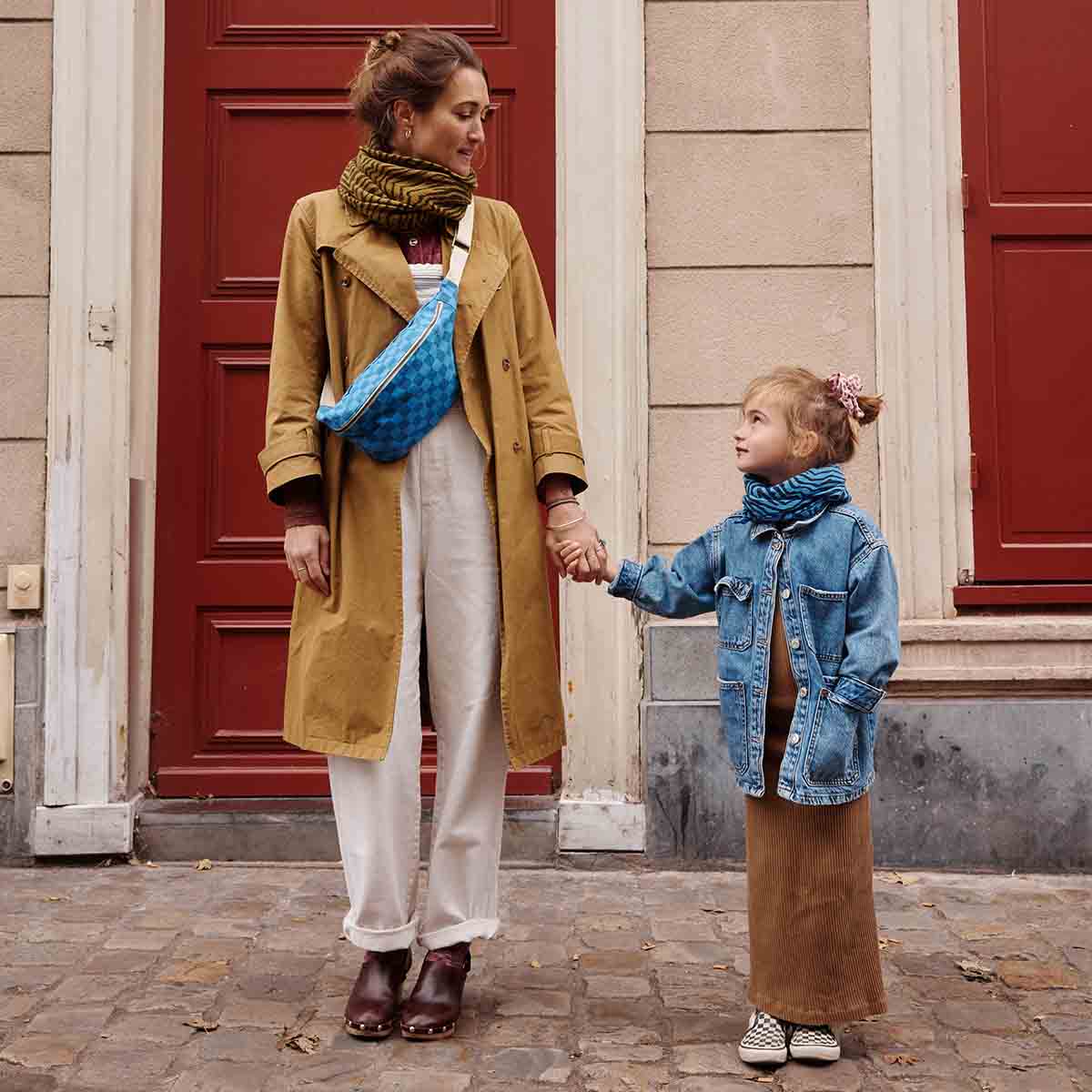 Woman and child holding hands in front of a building with red doors.