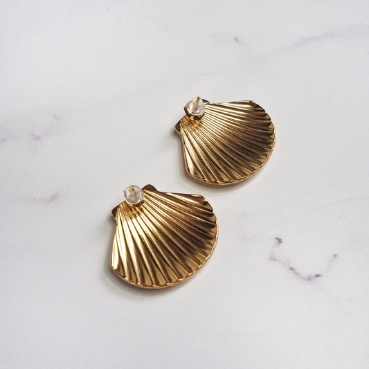 Gold shell-shaped earrings on a marble surface