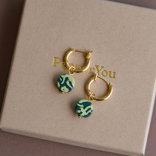 Gold hoop earrings with green patterned charms on a 'Peach & You' branded box.