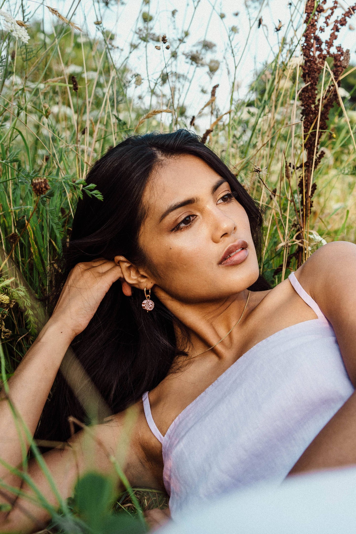 Woman in a light purple top sitting in a field of tall grass and wildflowers.