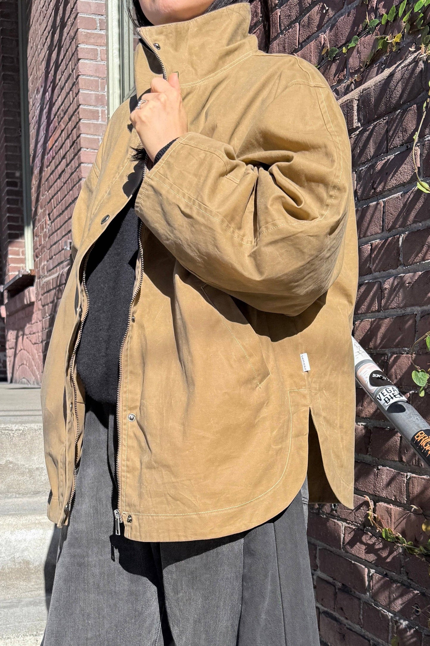 Person wearing a brown jacket standing against a brick wall.