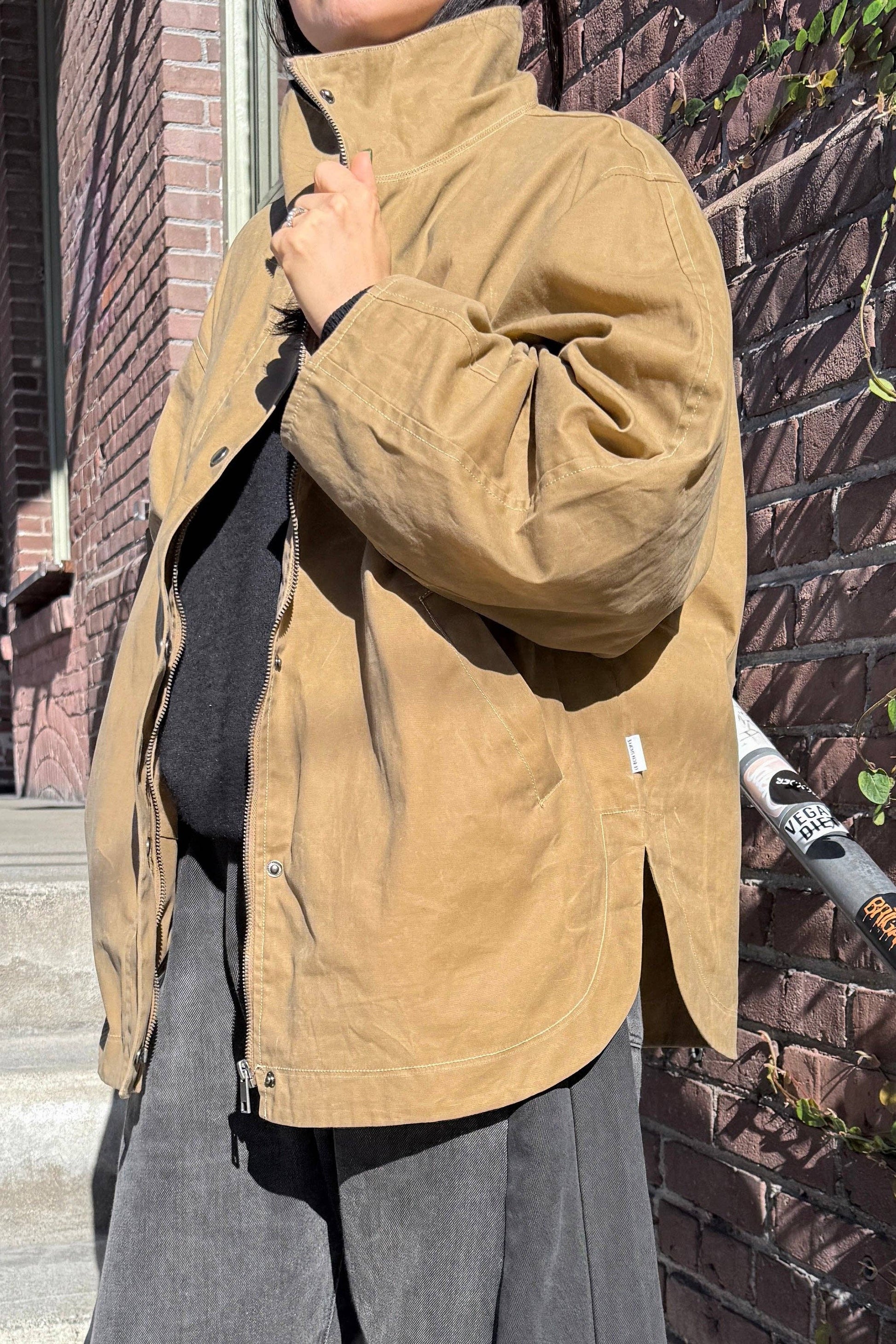 Person wearing a brown jacket standing against a brick wall.