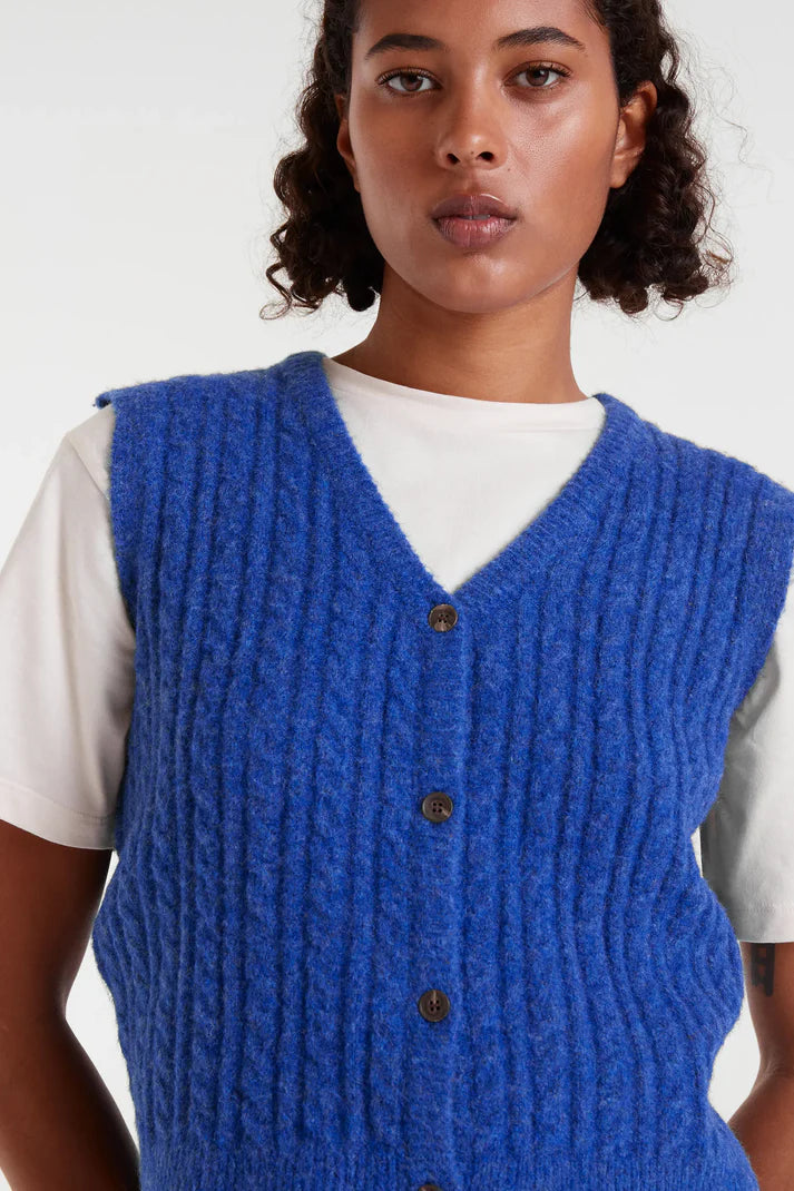 Person wearing a blue knitted vest over a white shirt on a plain background