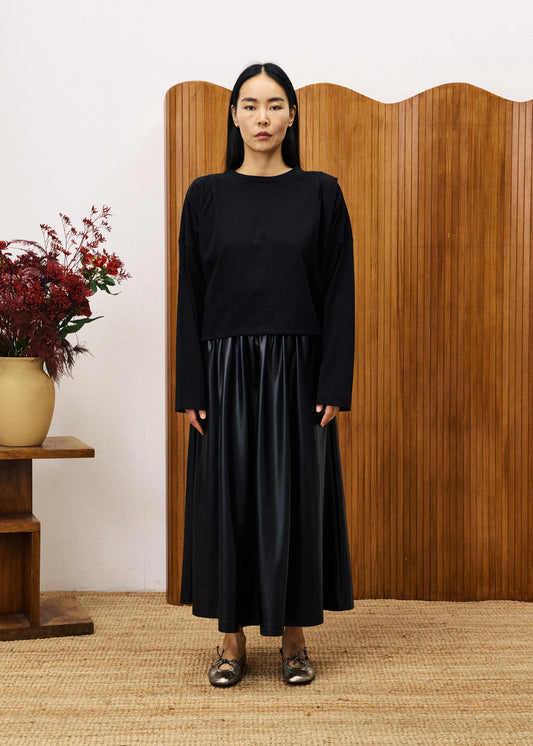 Person wearing a black outfit standing in front of a wooden screen with floral decorations.