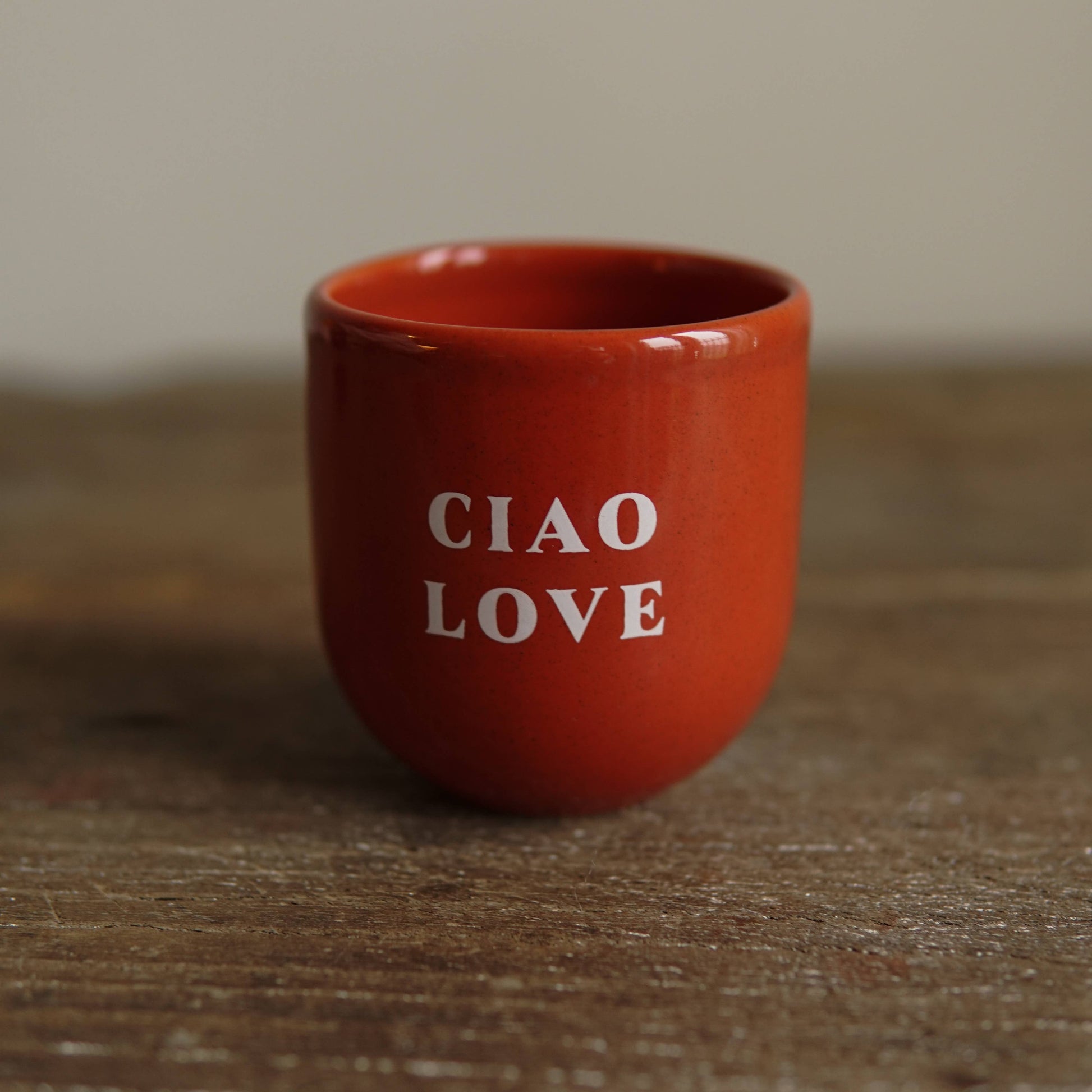 Red ceramic cup with 'CIAO LOVE' text on a wooden surface
